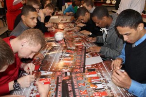 Members of the Hawks men's basketball team autograph the poster commemorating their 4th place finish in state this year.